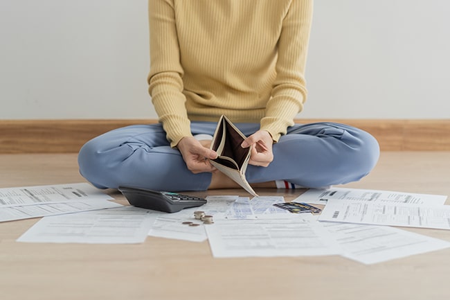 Kvinna sitter på golvet med räkningar och en tom plånbok.
